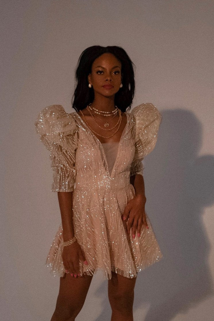 Model in a short champagne wedding dress with sculpted puff shoulders and a fitted bodice, layered necklaces, Soleil