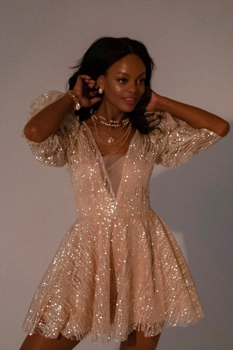 Close crop of a sparkling champagne mini wedding dress with a deep V neck and puffed sleeves, model smiling, Soleil