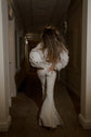 Back view of a bride walking down a hotel corridor in figure-hugging flared bridal trousers and a puff-sleeve jacket, Sun Flares