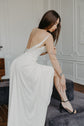 Model leaning on a velvet bench in a satin sample wedding dress, cowl back draped low and a black strappy heel, ZEPHYR Sample