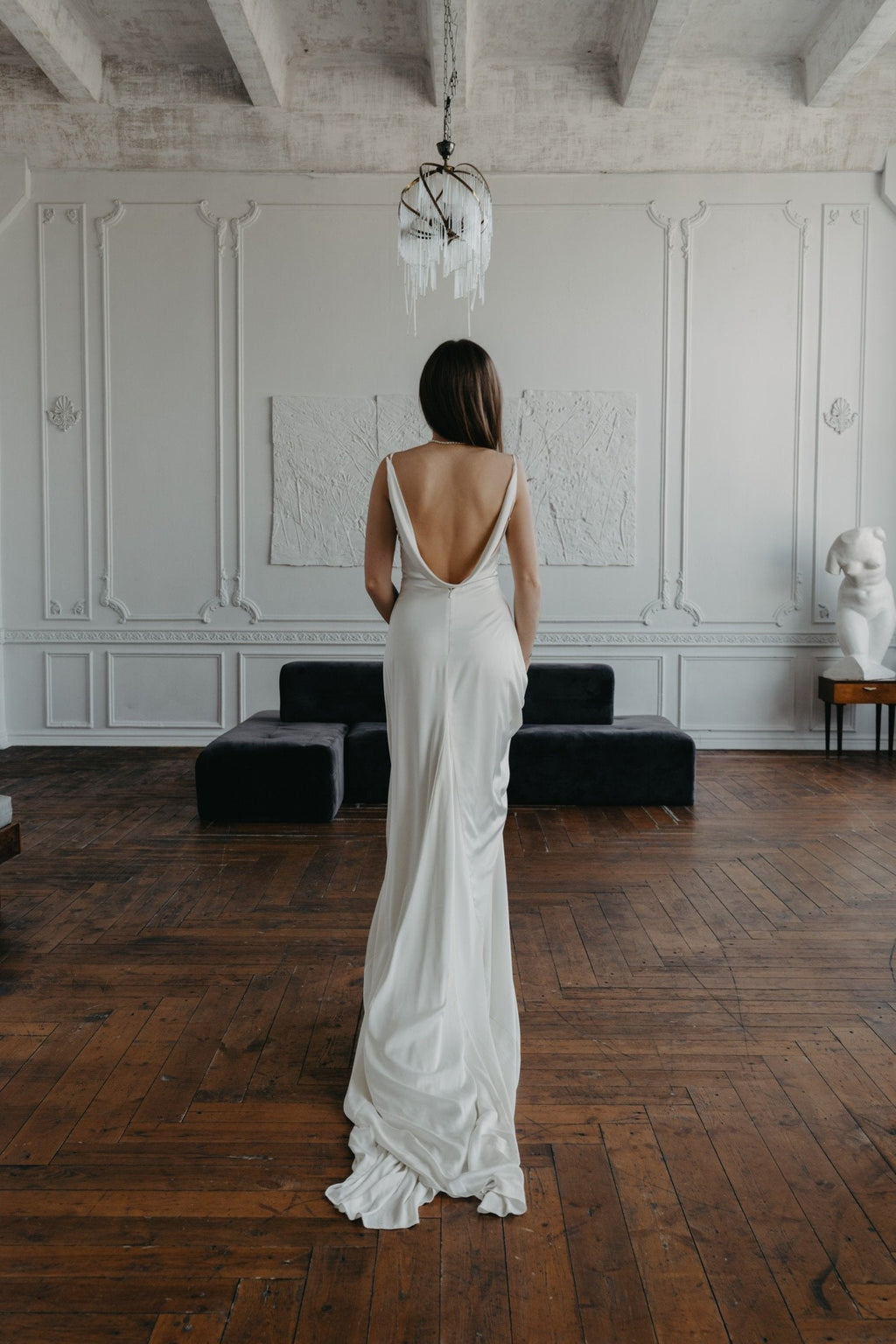 Full back view of a satin sample wedding dress with an open cowl back and pooled train, model in a white salon, ZEPHYR Sample