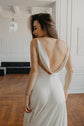 Close back view of a satin sample wedding dress with a deep draped cowl back and thin straps, model tossing her hair, ZEPHYR Sample