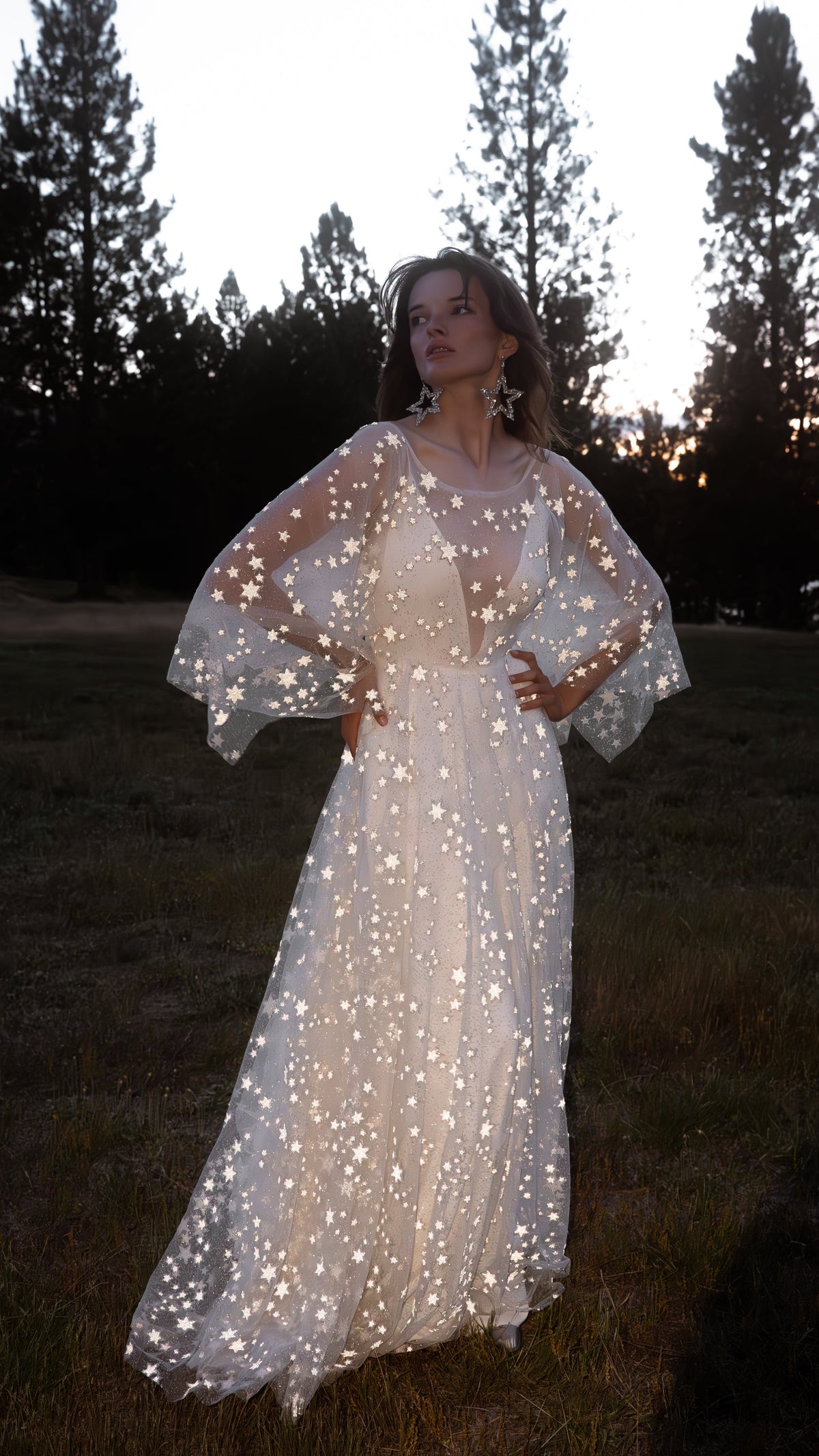Bride with hands on hips on a lawn at dusk, star lace wedding dress glowing under flash, Counting Stars Sample