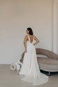 Satin sample wedding dress with thin straps and a draped cowl open back, model by a curved sofa, train on the floor, ZEPHYR Sample by Ephemeris