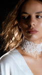 Bridal choker in milky ivory corded lace with a soft eyelash edge, worn close at the neck above a satin V neckline. Lyra Lace Choker by Ephemeris