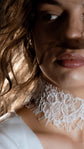 Tight crop of a lace bridal choker with a fringed lower edge, model glancing down in low warm light, Lyra Lace Choker