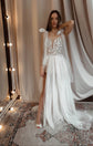 Bride with an arm raised under string lights, plunge star wedding dress with bow straps and a front slit, Make a Wish