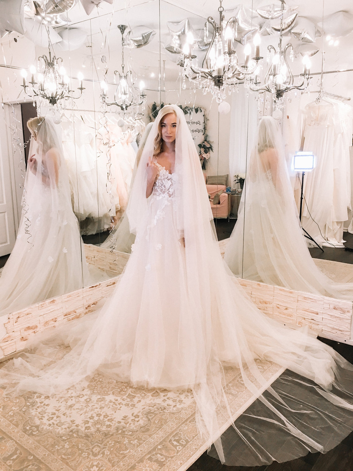 Cathedral length wedding veil spread across a rug in a mirrored bridal salon, bride under chandeliers, Cascade Veil