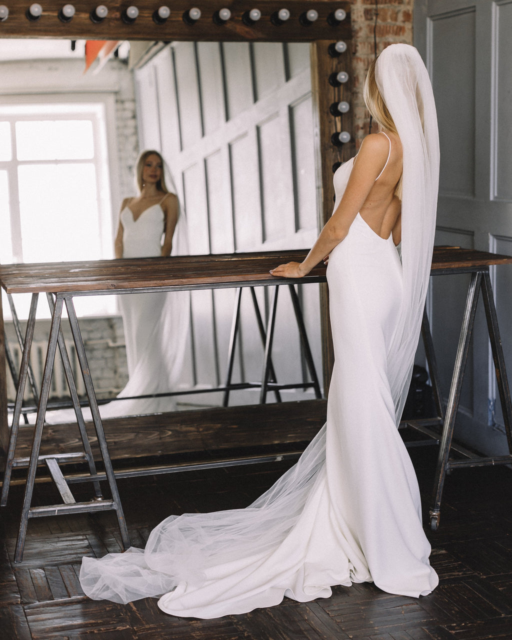 Back view of a cathedral wedding veil falling over a low-back crepe gown, bride facing a large studio mirror, Niagara Veil