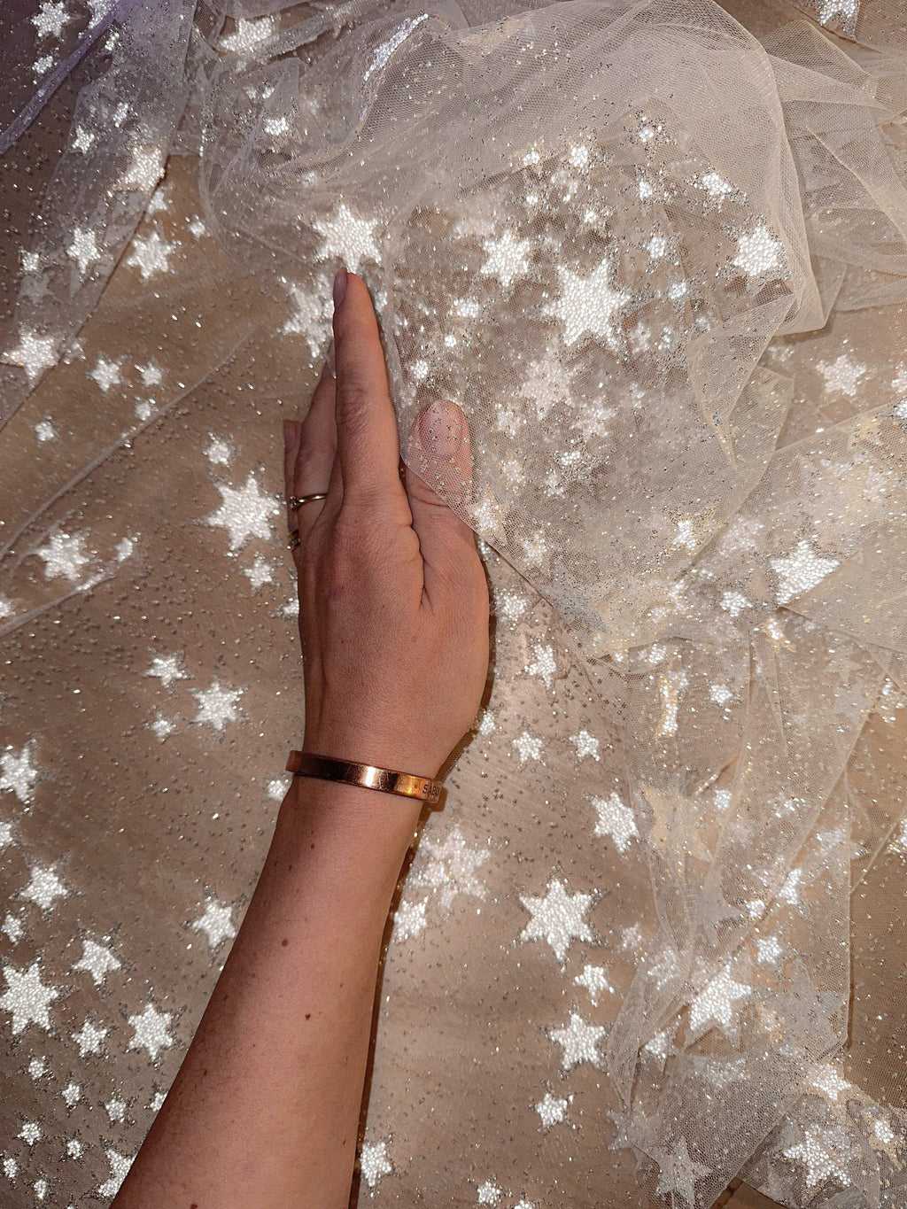 Star wedding veil detail, a hand resting on soft tulle with fine glitter and reflective stars, Milky Way Veil