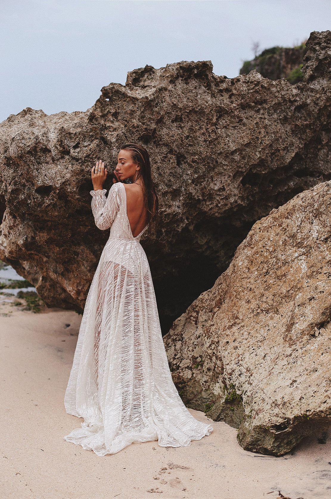 Bride between beach boulders, deep open back and sheer skirt of an ivory lace wedding dress over a short slip, Galaxy Ivory