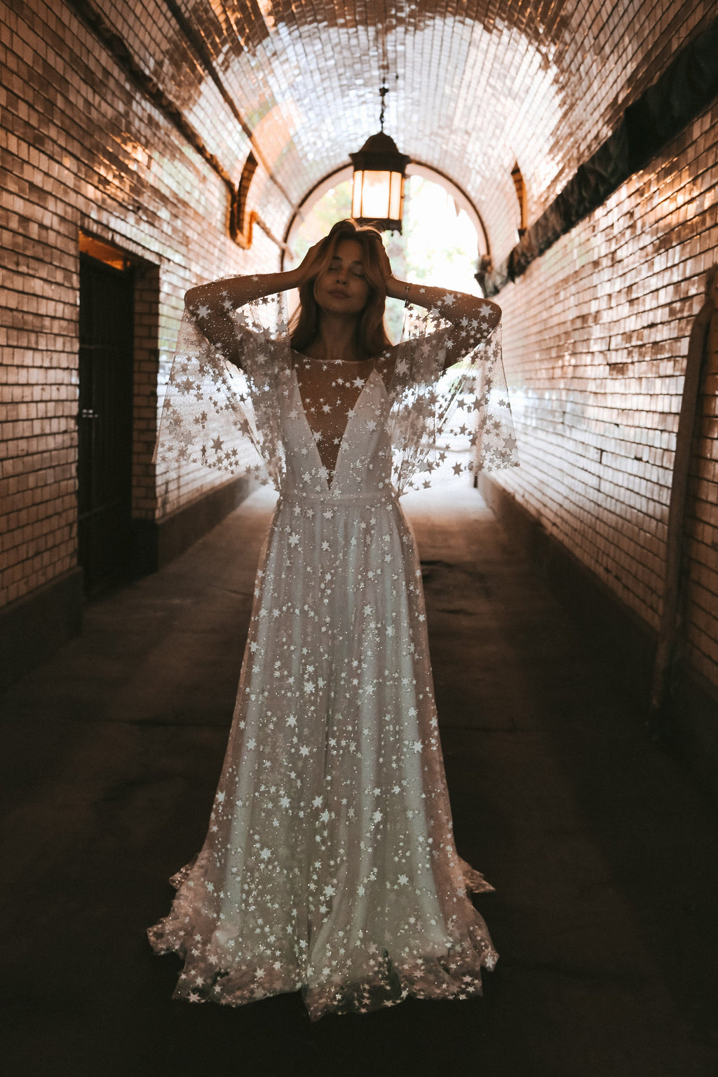Bride with hands in her hair, star lace wedding dress with a deep V-neck and wide sleeves in a lit tunnel, Counting Stars Sample