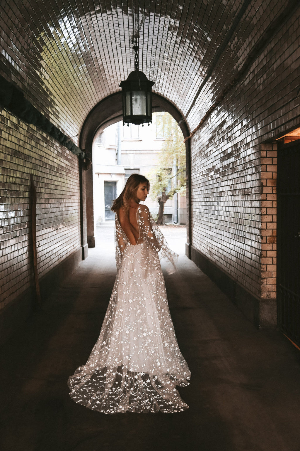Back view of a bride walking through a brick tunnel, open back star lace wedding dress and long train, Counting Stars