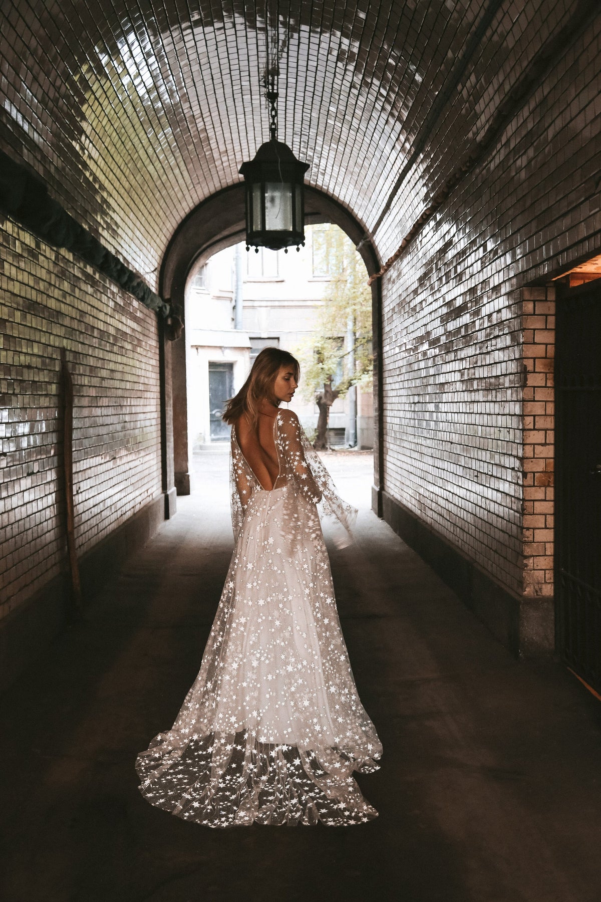 Back view of a bride walking down a tiled tunnel, open back star lace wedding dress and train, Counting Stars Sample