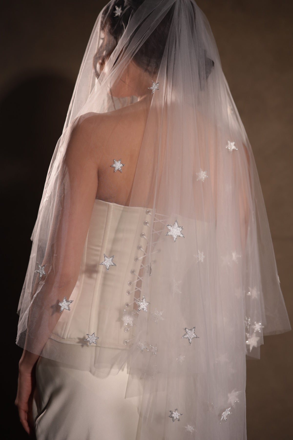 Detail from behind of a star-scattered two-tier wedding veil falling over laced corset buttons, soft studio light, Celestial Glow Veil