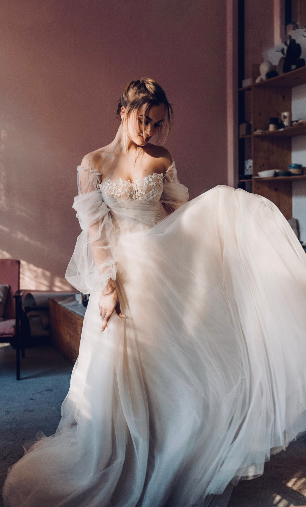 Bride swirling the full skirt of an off-shoulder tulle wedding dress with sheer puff sleeves, warm studio, Savanna