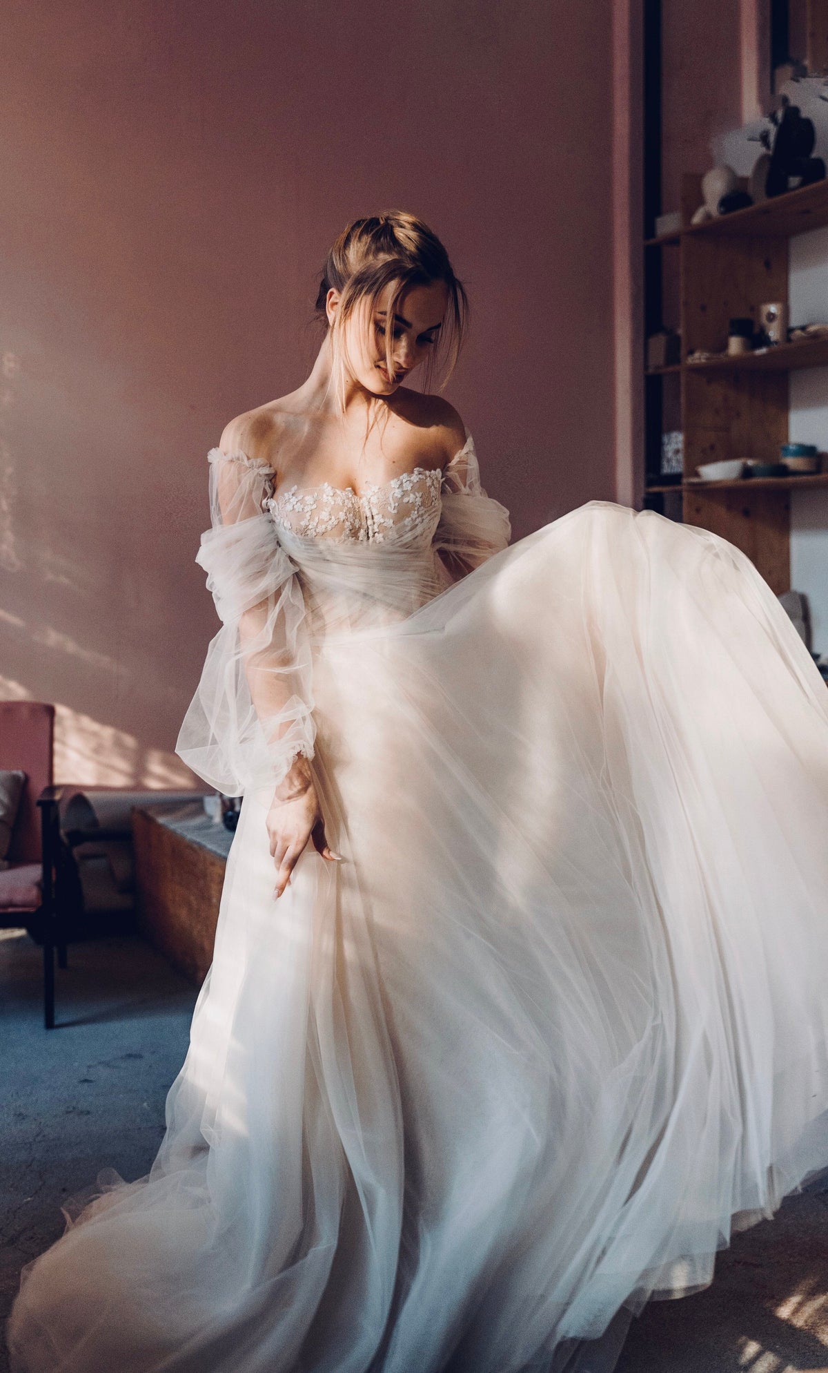 Bride swirling the full skirt of an off-shoulder tulle wedding dress with sheer puff sleeves, warm studio, Savanna