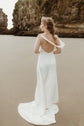 Back view of a bride on the sand in a satin sample wedding dress, one strap slipped and the cowl back open, train behind, ZEPHYR Sample