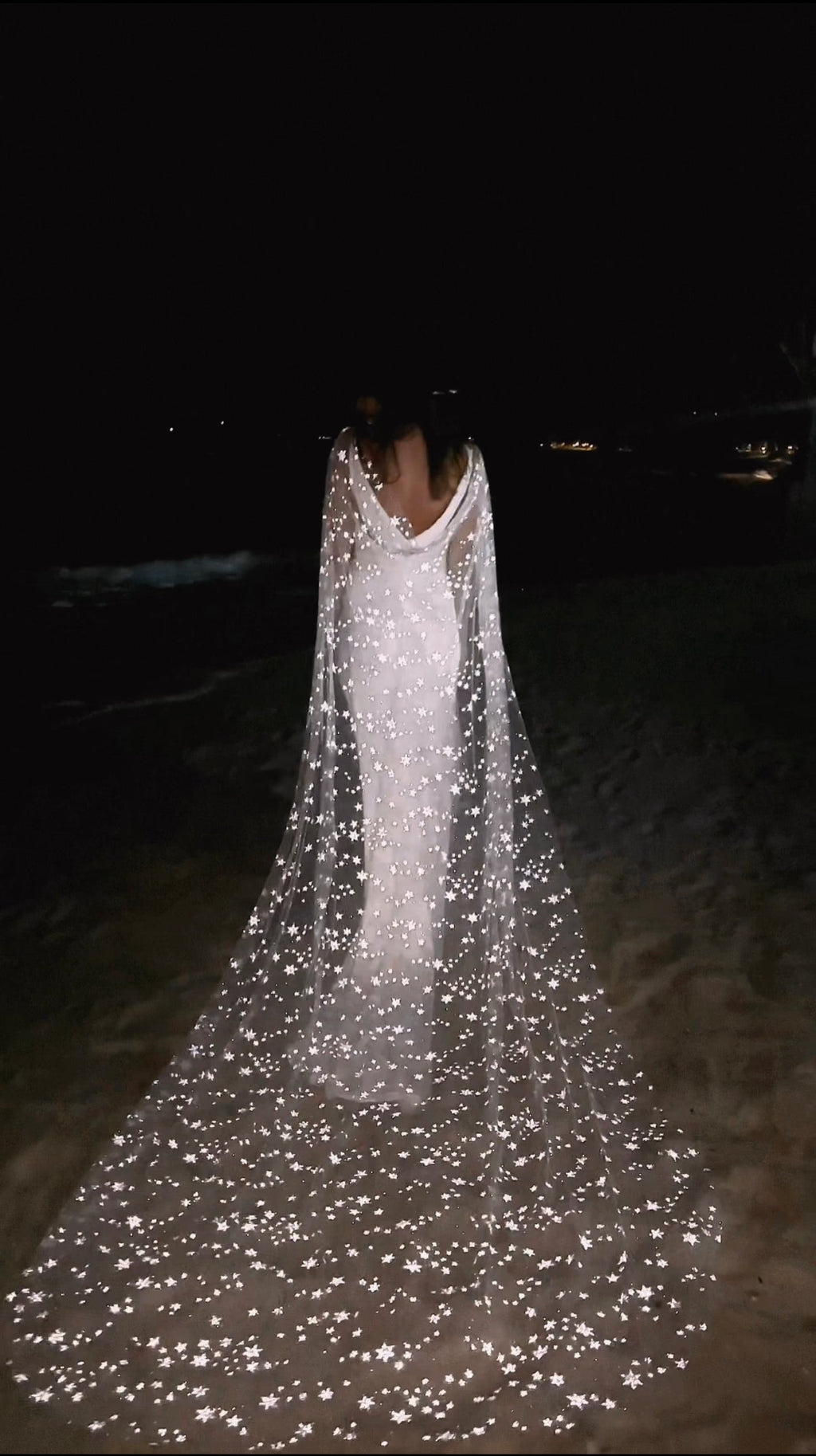 Star-scattered bridal cape trailing across the sand at night, stars catching the light behind a bride, Milky Way Cape Black by Ephemeris