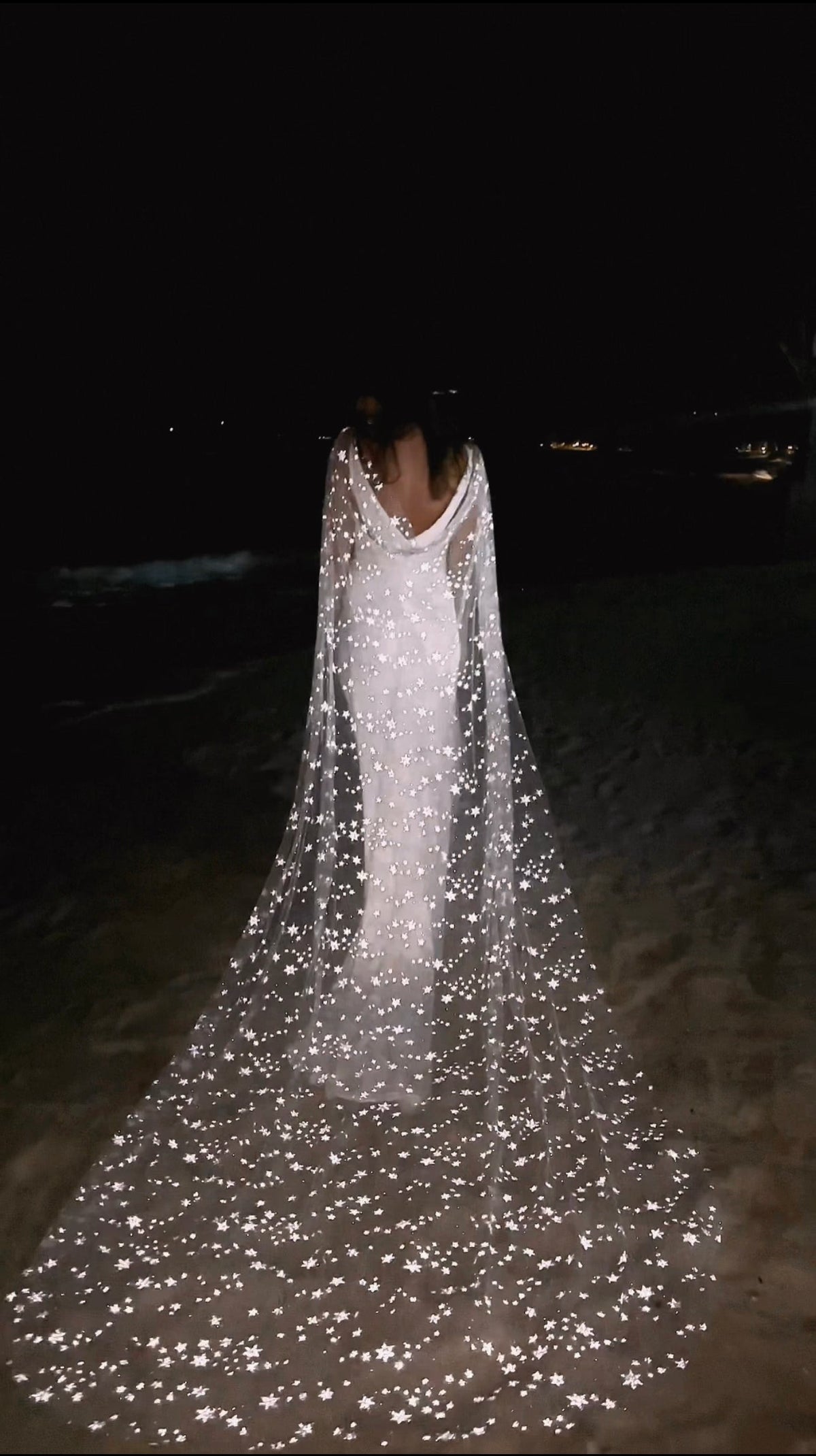 Star-scattered bridal cape trailing across the sand at night, stars catching the light behind a bride, Milky Way Cape Black by Ephemeris