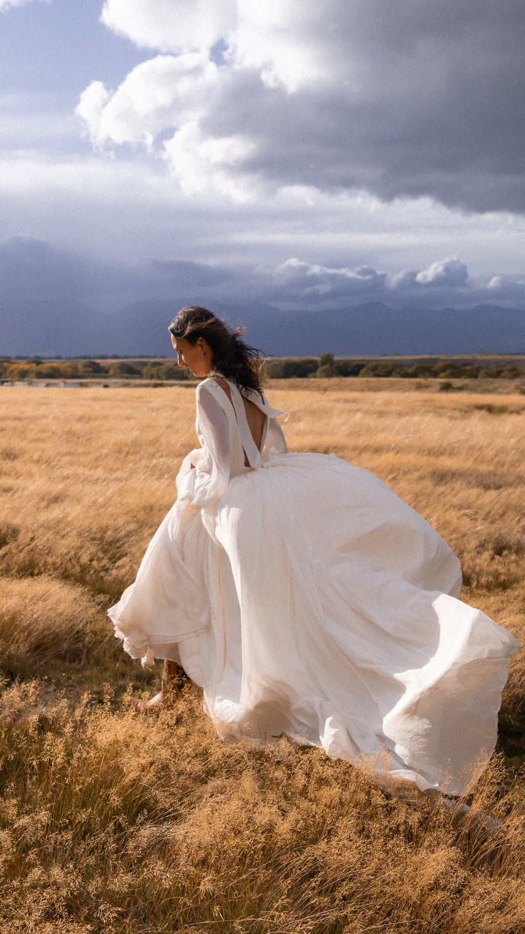 Bride running through golden grass under storm clouds, open-back chiffon wedding dress billowing behind her, When the Moon is Out