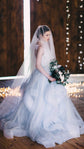 Two-tier cathedral wedding veil in soft tulle worn over the face, bride with a bouquet in a candlelit barn. Cascade Veil by Ephemeris