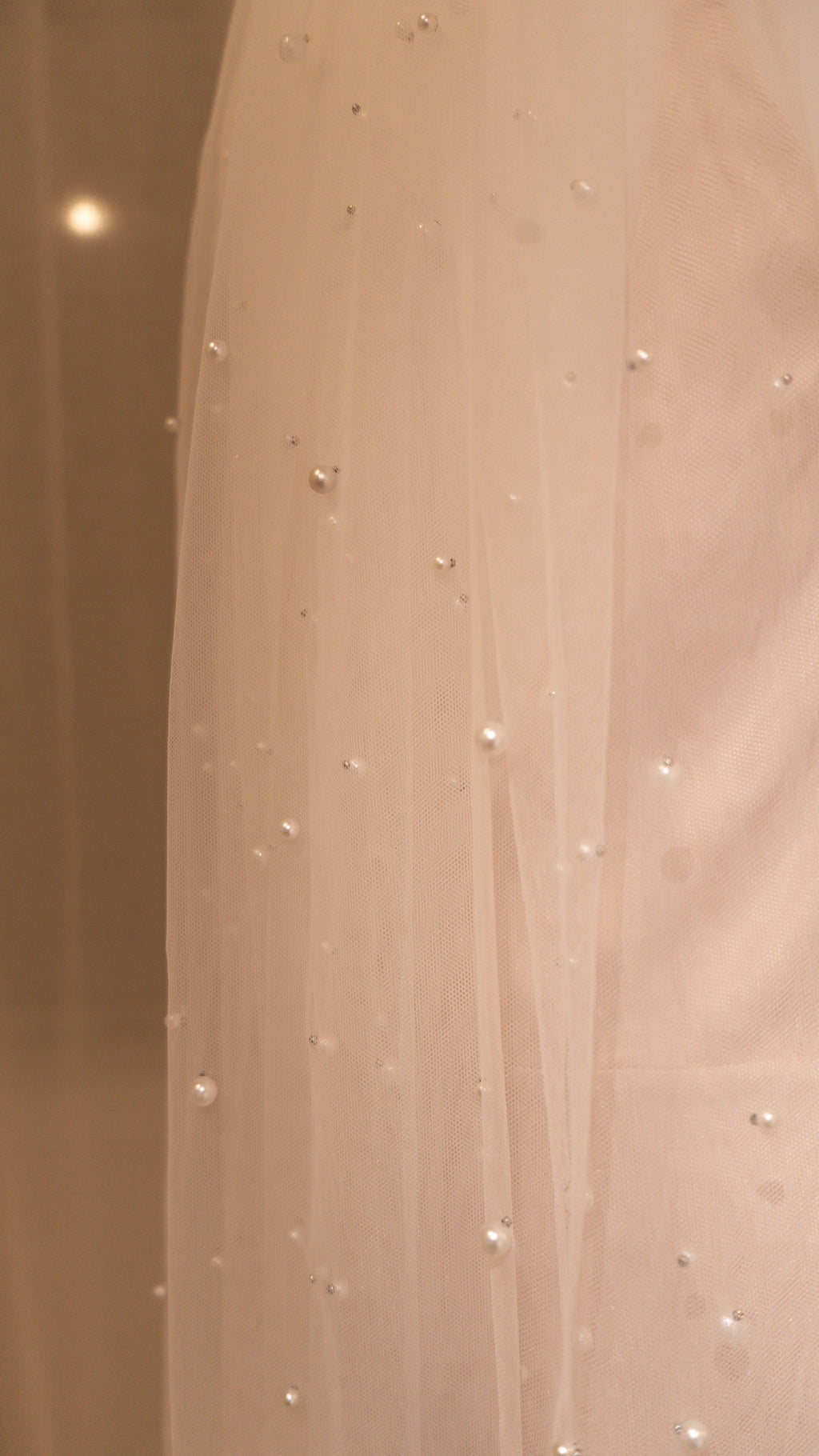 Close-up of pearls placed across soft tulle on a cathedral wedding veil, warm blush backdrop, Pearl Cascade Veil