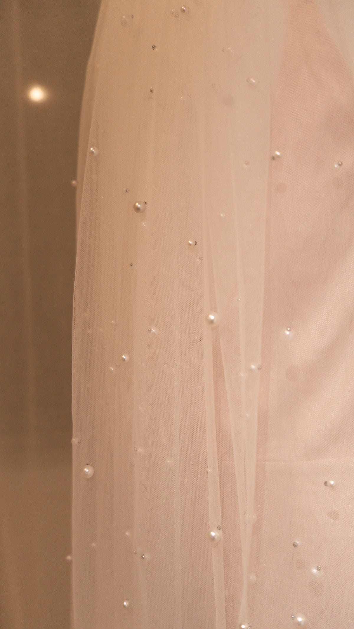 Close-up of pearls placed across soft tulle on a cathedral wedding veil, warm blush backdrop, Pearl Cascade Veil