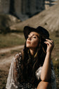 Bride in a black hat and star lace wedding dress, eyes closed in warm light, sheer starry sleeve at her shoulder, ASH Counting Stars