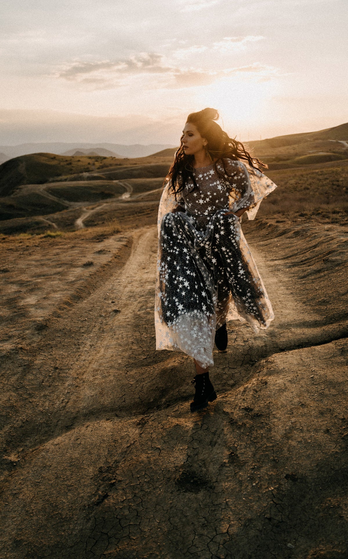 Full-length bride walking a dirt road in boots, black and ivory star lace wedding dress blowing at sunset, ASH Counting Stars
