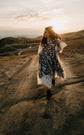 Full-length bride walking a dirt road in boots, black and ivory star lace wedding dress blowing at sunset, ASH Counting Stars