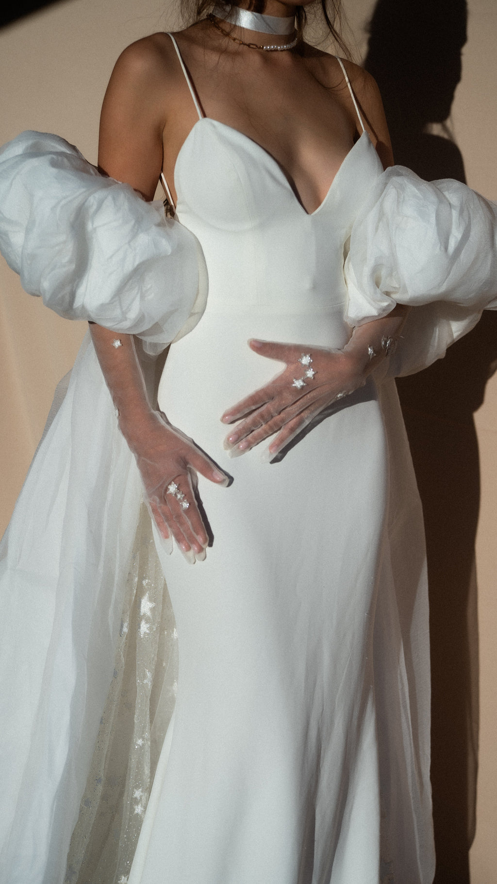 Cropped view of an ivory bridal cape with puff sleeves over a slip gown, sheer star gloves resting on the waist, Aura Cape