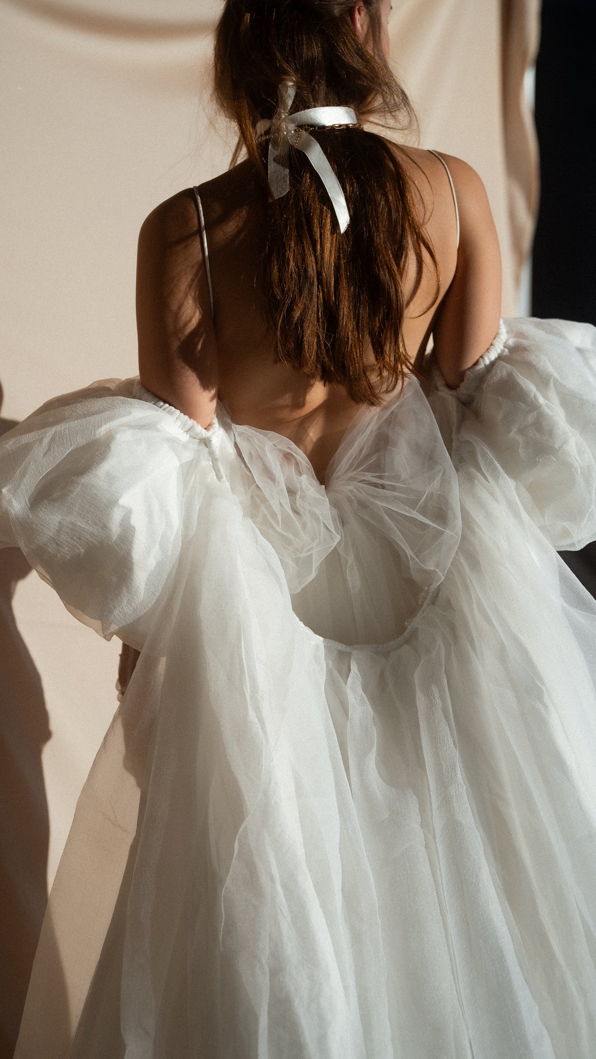 Close-up from behind of crinkled chiffon puff sleeves and the draped back of an ivory bridal cape, bride with a hair ribbon, Aura Cape