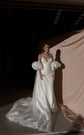 Ivory bridal cape with puff sleeves over a slip gown, chiffon train curving across a studio floor in low light, Aura Cape