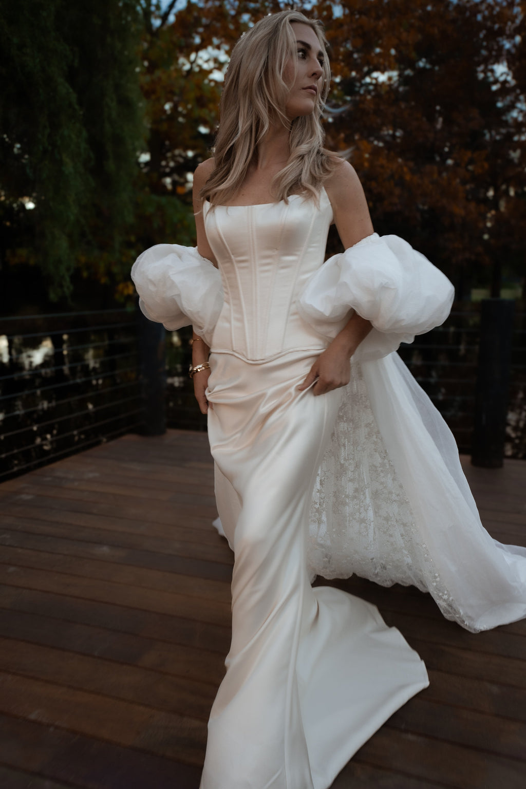 Bride walking on a wooden deck in an ivory bridal cape with puff sleeves, star lace showing under the chiffon train, Aura Cape