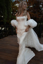 Bride walking on a wooden deck in an ivory bridal cape with puff sleeves, star lace showing under the chiffon train, Aura Cape