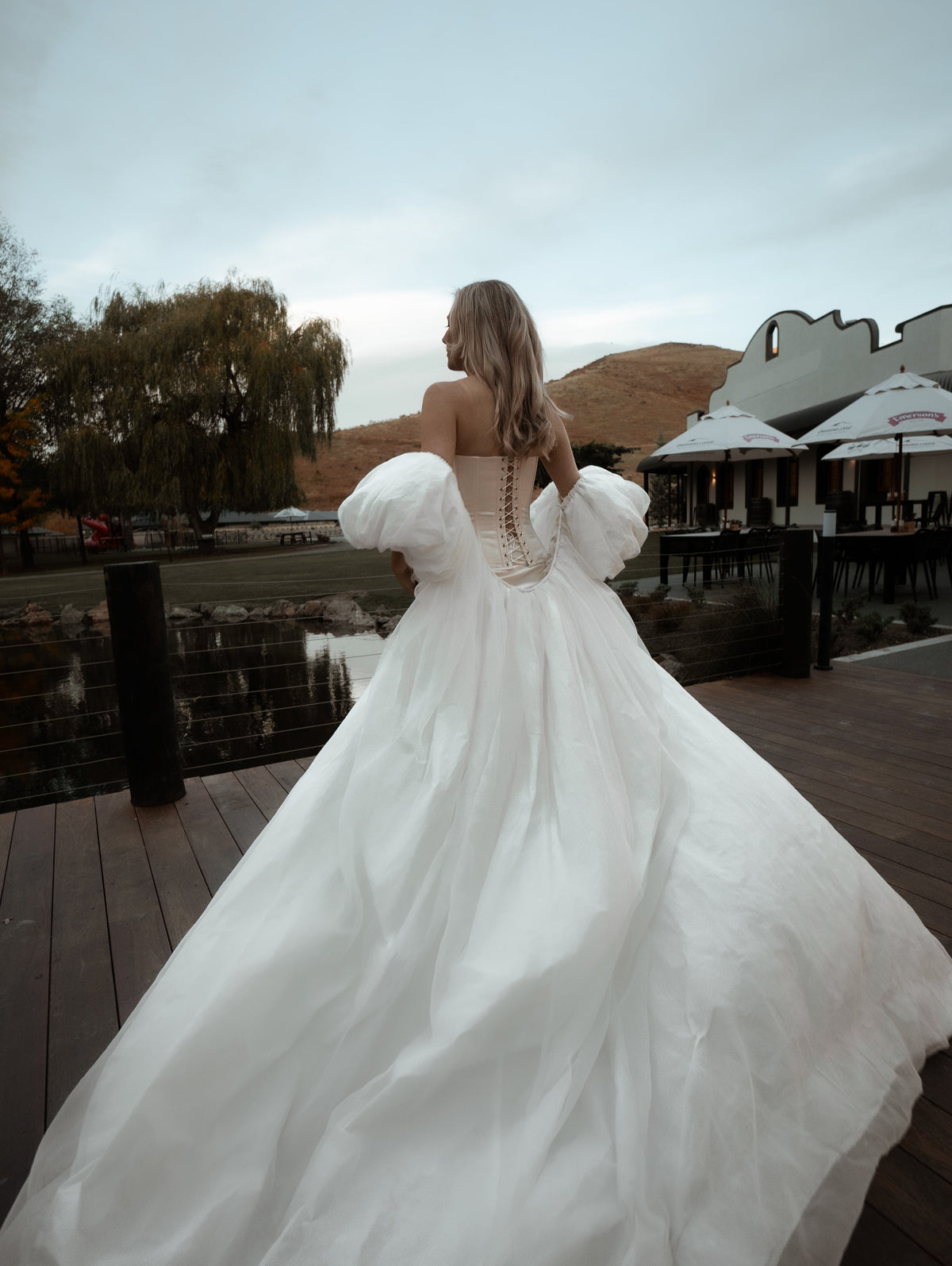 Back view of a bride on a terrace, ivory bridal cape with puff sleeves billowing into a full chiffon train, Aura Cape
