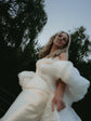 Playful low-angle shot of a laughing bride in motion, ivory bridal cape puff sleeves swinging against the trees, Aura Cape