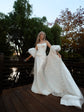 Bride on a deck by a pond, ivory bridal cape with puff sleeves and a long star-dotted train stretched across the boards, Aura Cape