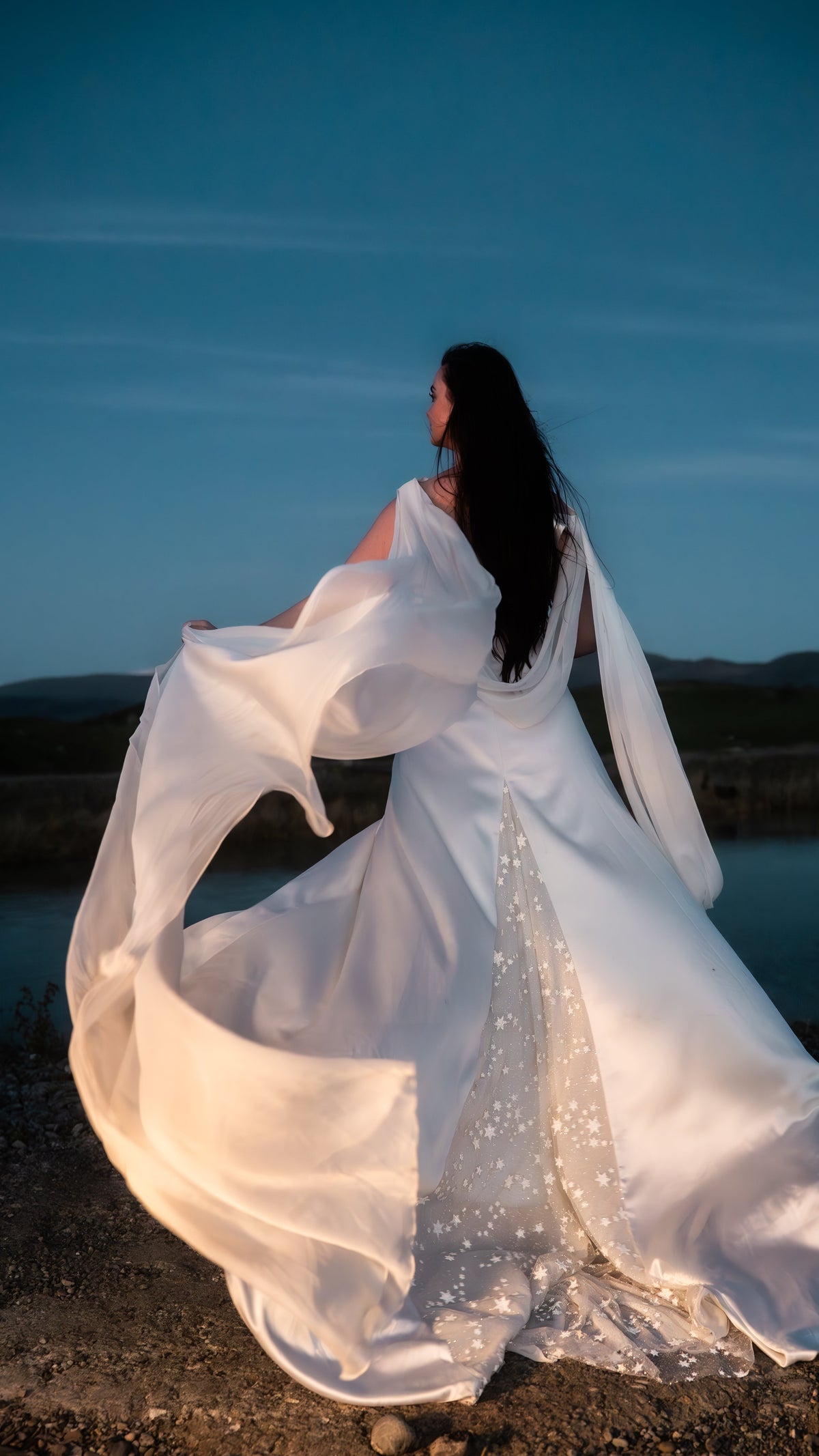 Bride twirling a satin wedding dress at dusk, chiffon wing caught in the wind and star-scattered train swirling, Aurora