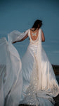 Wind lifting a chiffon wing off a satin open back wedding dress, butterfly embroidery and star train at blue hour, Aurora