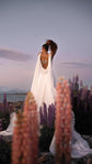 Open back wedding dress with a butterfly on the back, seen through pink lupines at dusk by a lake, Aurora