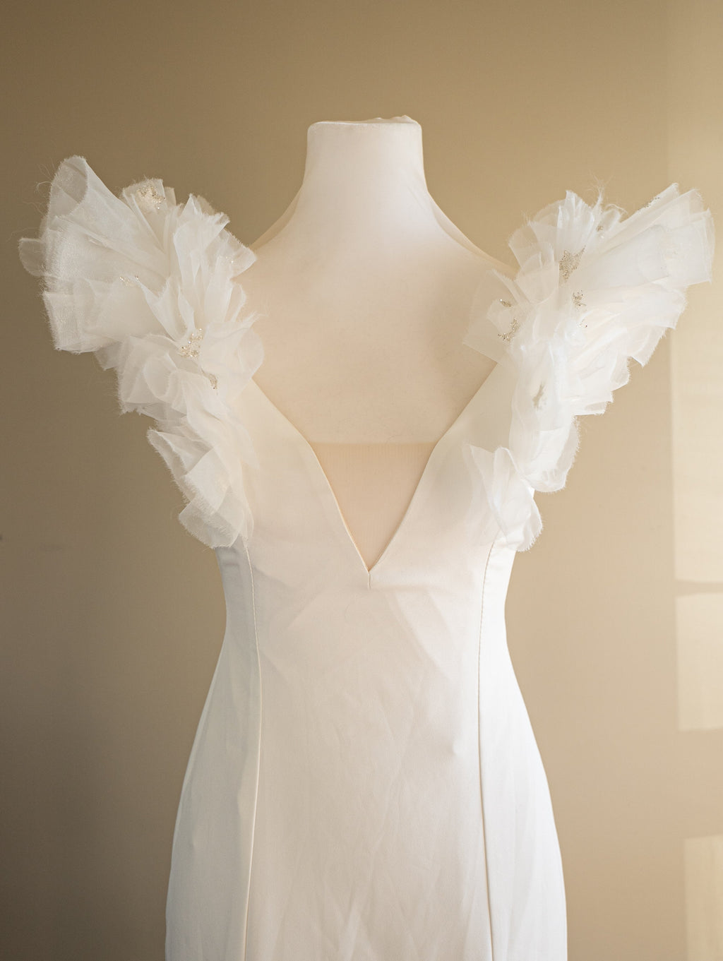 Close-up on a dress form of a crepe sample wedding dress, deep V-neck with sheer panel and ruffled tulle shoulders, Celeste Sample