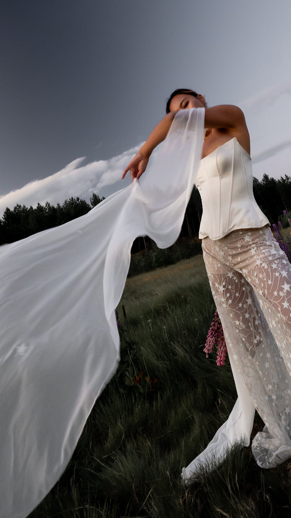 White chiffon bridal scarf caught by the wind and stretched wide, bride in a corset and star trousers in a field, Celeste Scarf