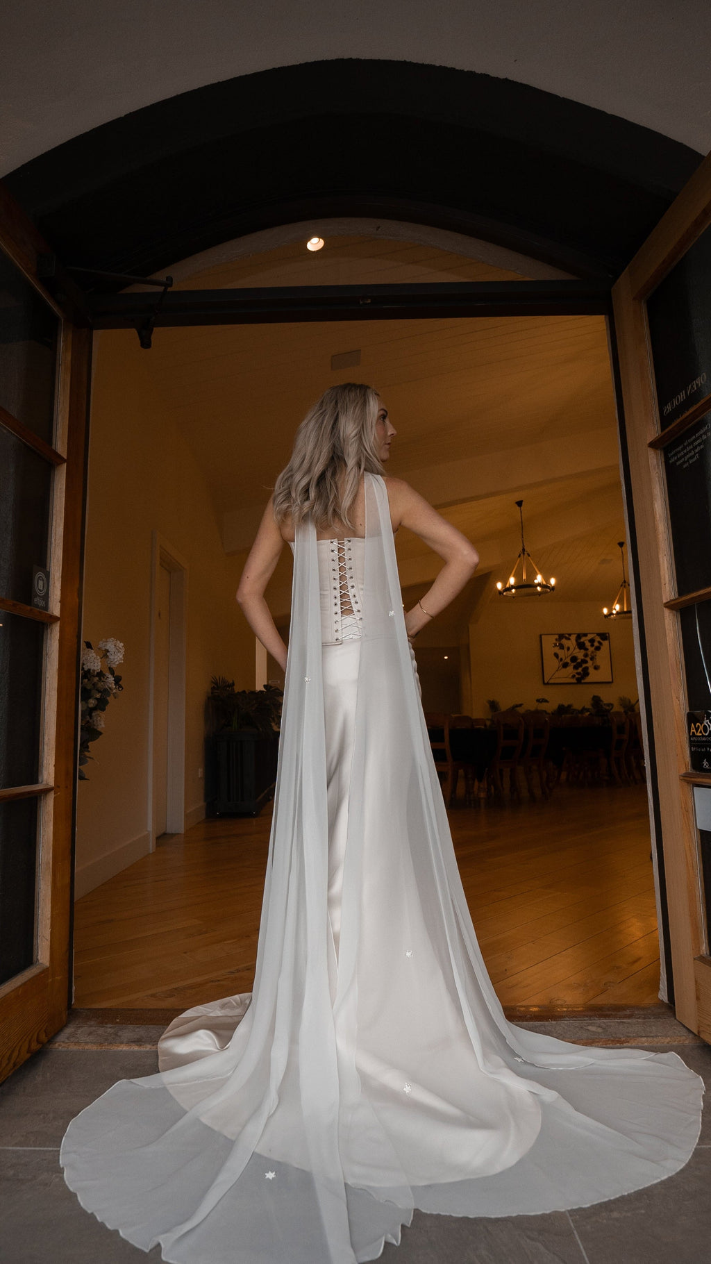 Back view in an arched doorway, chiffon bridal scarf falling from the neck to a long sweep on the floor, Celeste Scarf