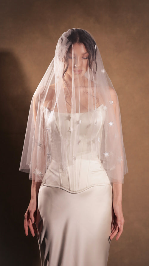 Two-tier star wedding veil with the blusher worn over the face, hand-placed stars on soft white tulle, satin corset gown. Celestial Glow Veil by Ephemeris