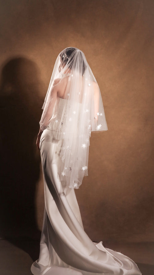 Side view of a celestial wedding veil with blusher down over a satin gown with a long train, warm brown studio backdrop, Celestial Glow Veil