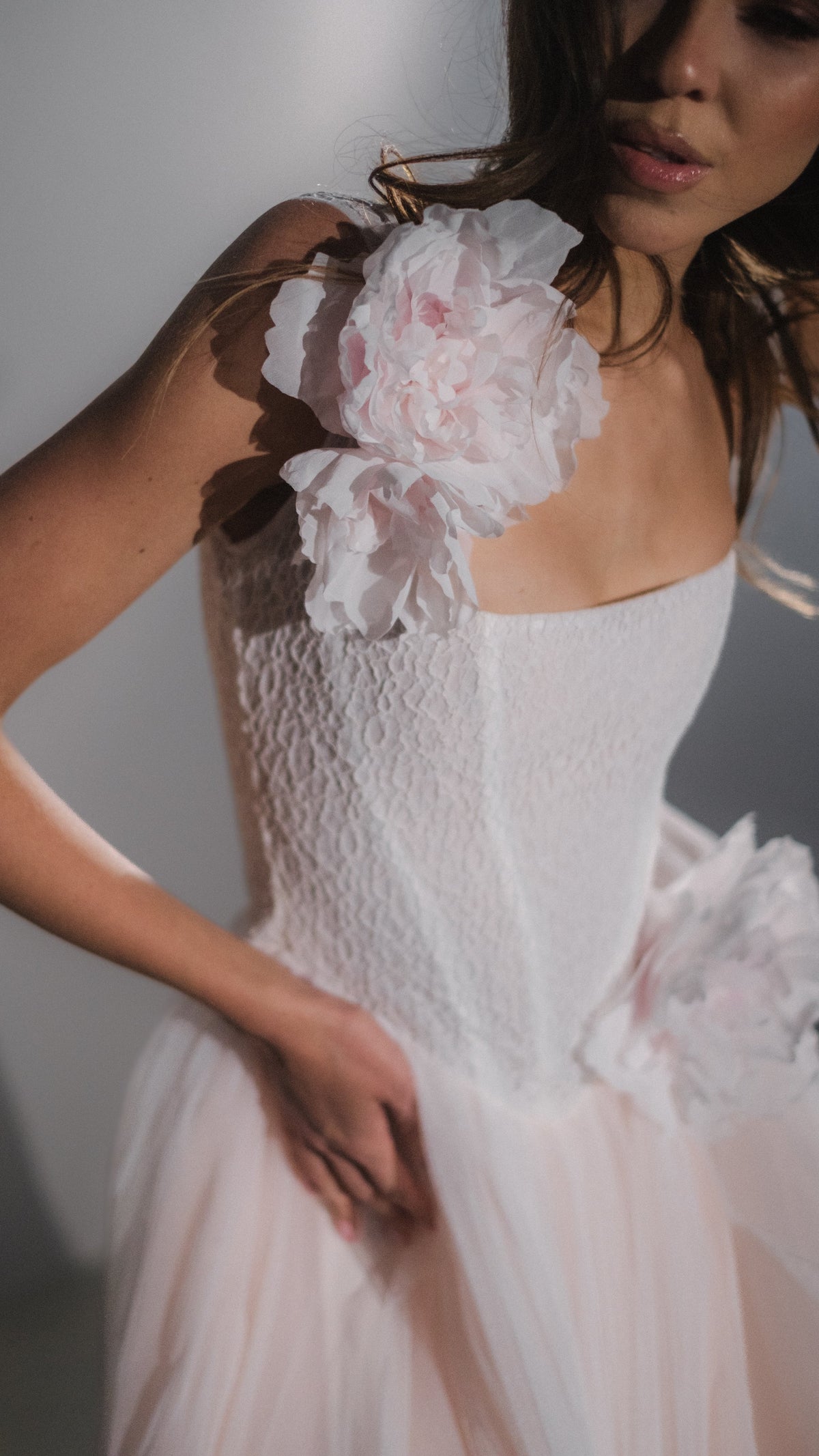Blush corset wedding dress with a textured lace bodice, dropped waist and silk flowers at the shoulder and hip, close crop. Chrysanthemum by Ephemeris