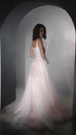 Three-quarter back view of a blush pink wedding dress with laced corset and long tulle train in an arched alcove, Chrysanthemum