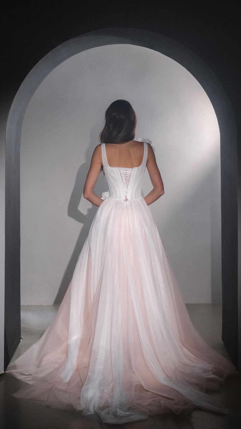 Full back view of a corset wedding dress with lace-up back and wide two-tone tulle skirt, model facing an arch, Chrysanthemum